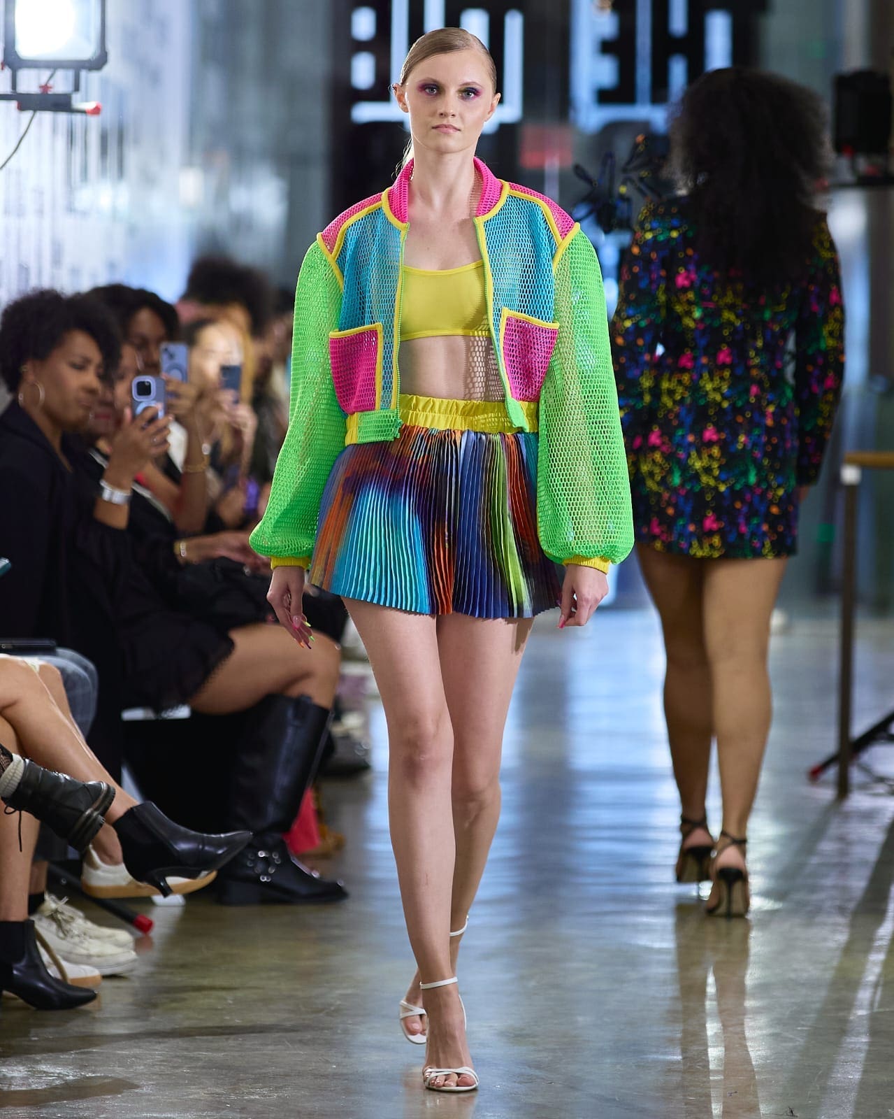 A model showcases a vibrant, colorful jacket while walking down the runway.