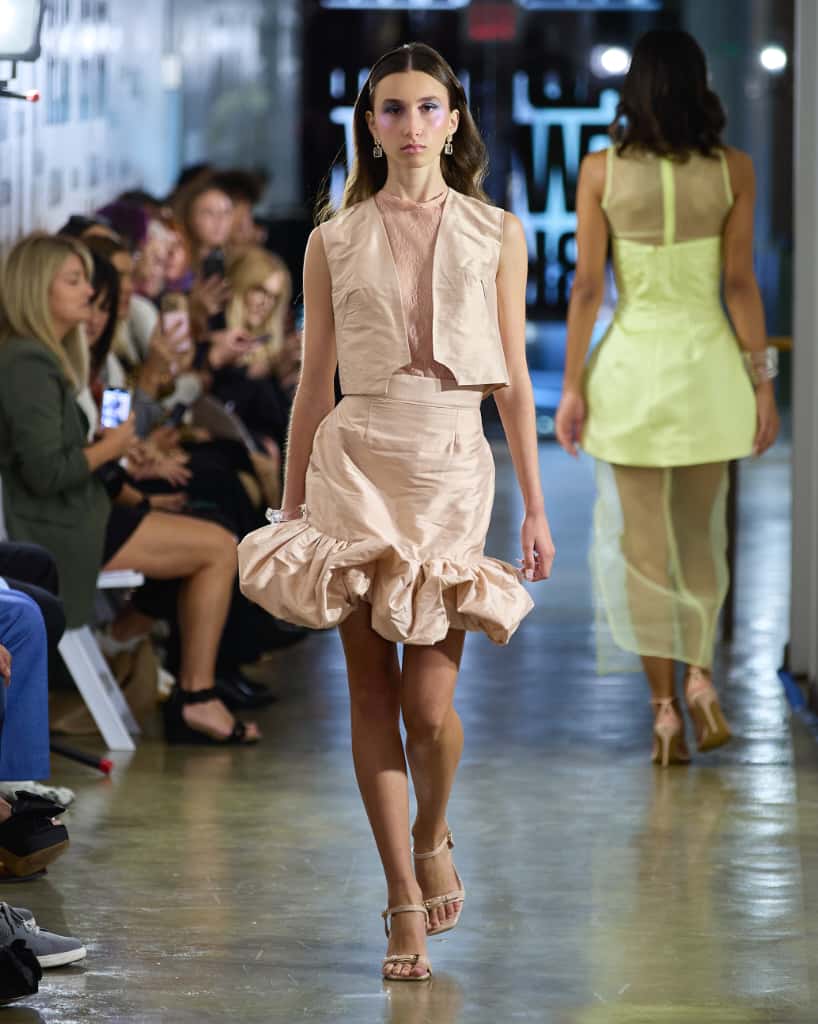 A model confidently walks the runway, showcasing a vibrant pink dress that flows elegantly with each step.